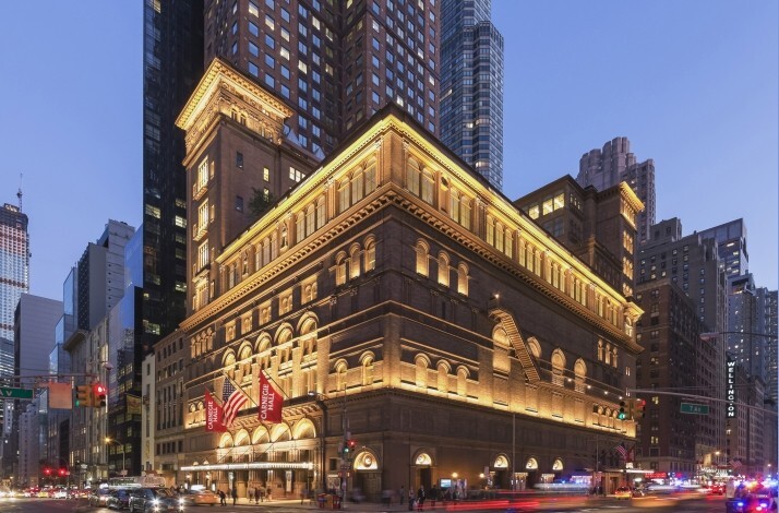 Illuminated exterior of Carnegie Hall at night with street traffic. 