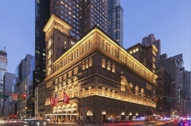 Illuminated exterior of Carnegie Hall at night with street traffic. 