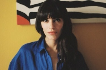 Coco Dávez poses for a photo against a yellow background.