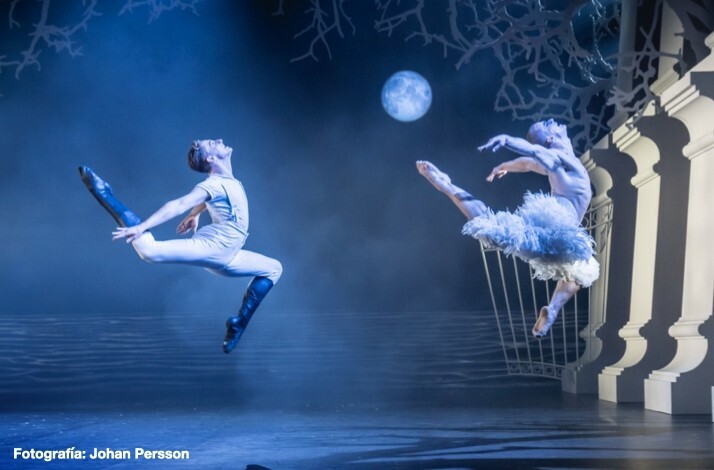 Two dancers from Matthew Bourne's Swan Lake mid-air, one in white attire and one in a swan costume, with a moonlit backdrop, gate, and columns. Fotografía: Johan Persson