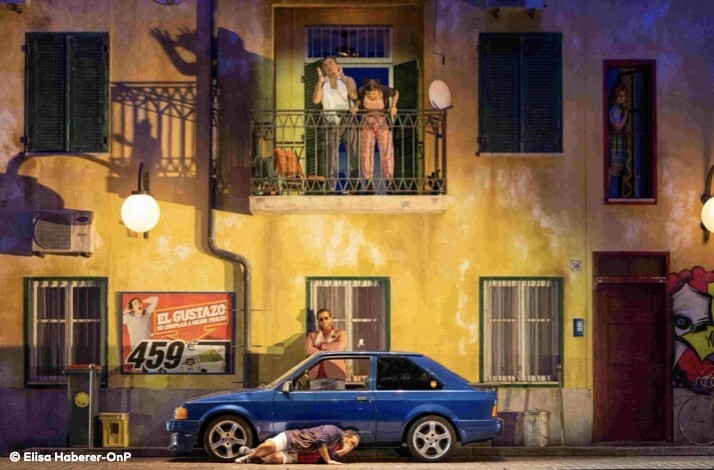 Performance of Il Barbiere di Siviglia on a modern street-facade opera stage next to a blue car. Photo by Elisa Haberer