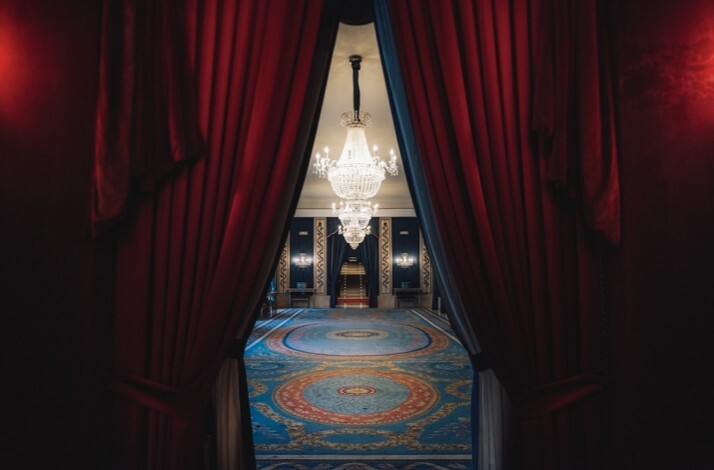 Ornate hall with red curtains, blue carpet, and grand chandeliers at Teatro Real.