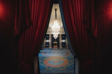 Ornate hall with red curtains, blue carpet, and grand chandeliers at Teatro Real.