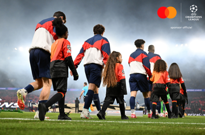 Players and child mascots walk out from the tunnel toward the pitch at a UEFA Champions League stadium, image captured from the below ground.