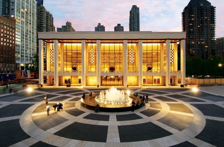 David H. Koch Theater at Lincoln Center lit up at dusk, with a fountain in the plaza.