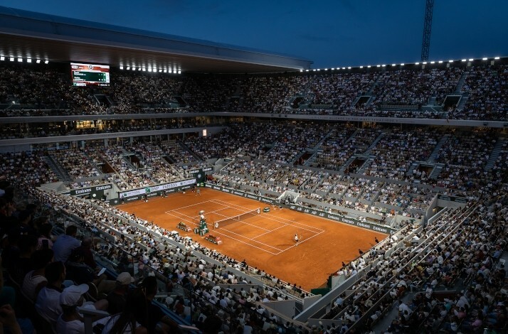 A fan's wide view of a live tennis game in Roland-Garros stadium, filled with fans and an open telescopic roof.