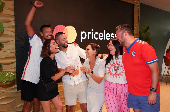 Group celebrates with drinks in front of the Mastercard Priceless lounge sign.