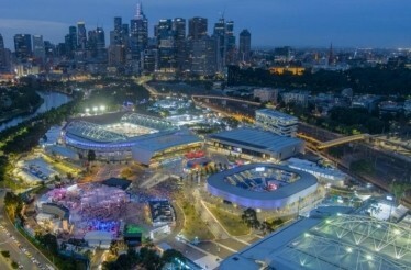 Tennis stadiums and courts illuminated at night with city skyline in the background.