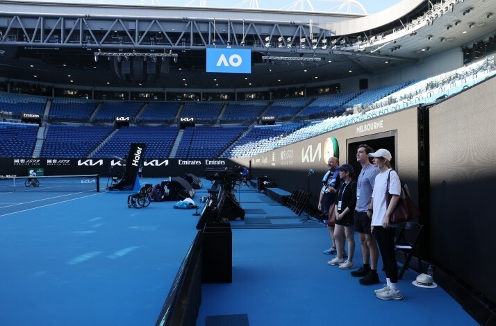 A group of people standing outside the field in an empty Rod Laver Arena, Melbourne.