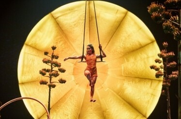 A person performing a trapeze act against a backdrop of golden circular light at Cirque du Soleil's LUZIA.