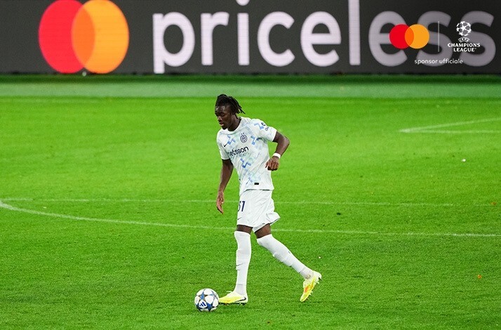 Inter Milan's player in white away kit advancing with the ball at night. Mastercard and UEFA Champions League logos at the top right corner.