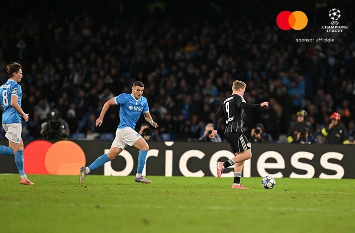 Three players on the field during UEFA Champions League match with priceless logo on the banner in the background.