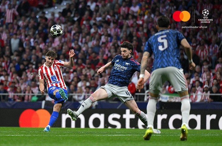 Atletico de Madrid player shooting across Declan Rice of Arsenal during a UEFA Champions League match. Mastercard and UEFA Champions League logos at the top right corner.