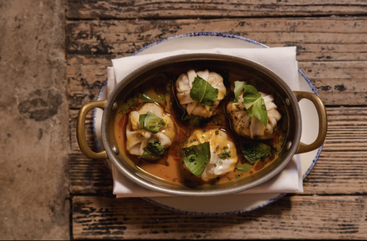 Pleated dumplings garnished with fresh herbs and chives in a rich, spiced broth, reflecting Si! Mon's Panamanian culinary influences.