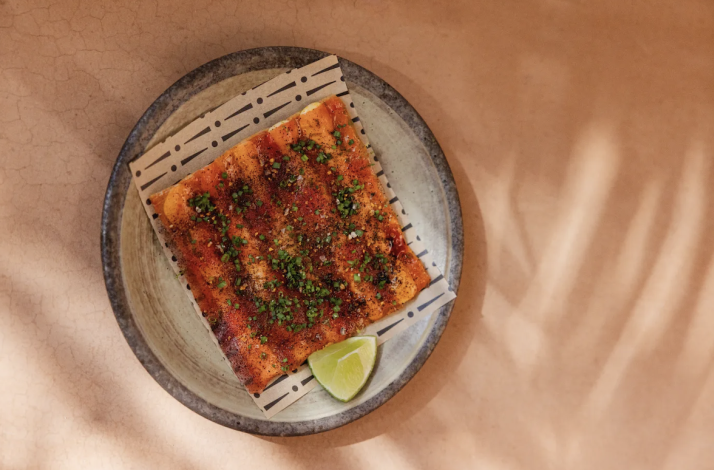 Overhead view of a chili-glazed flatbread garnished with herbs and lime, plated on a decorative bamboo mat at Si! Mon, Venice.