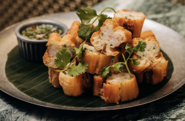 Golden fried bread cubes stacked on a banana leaf, garnished with cilantro and served with dipping sauce at Crying Tiger Chicago.