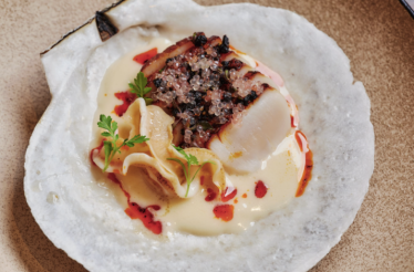 Seared scallop topped with caviar and charred elements, plated over cream sauce in a natural scallop shell at Uchi West Hollywood.