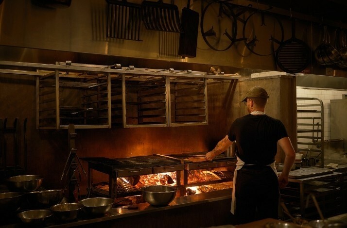 Antico Nuovo's Cook is grilling over an open flame in a rustic, professional kitchen