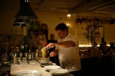 Antico Nuovo's Chef plating pasta in a cozy, warmly lit restaurant kitchen 