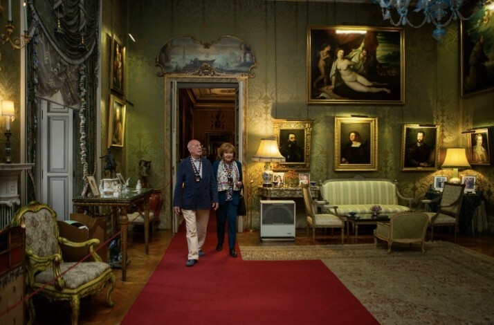 Two visitors walking on a red carpet in an elegant room adorned with classic paintings, antique furniture, and ornate decor at Liria Palace.