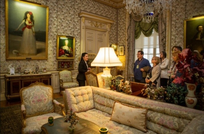 Visitors in a lavishly decorated room filled with detailed paintings and luxurious furnishings