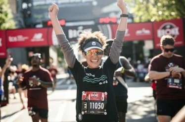 A runner with her arms raised in celebration stands out amidst a crowd of runners, after completing the Bronx New York run.