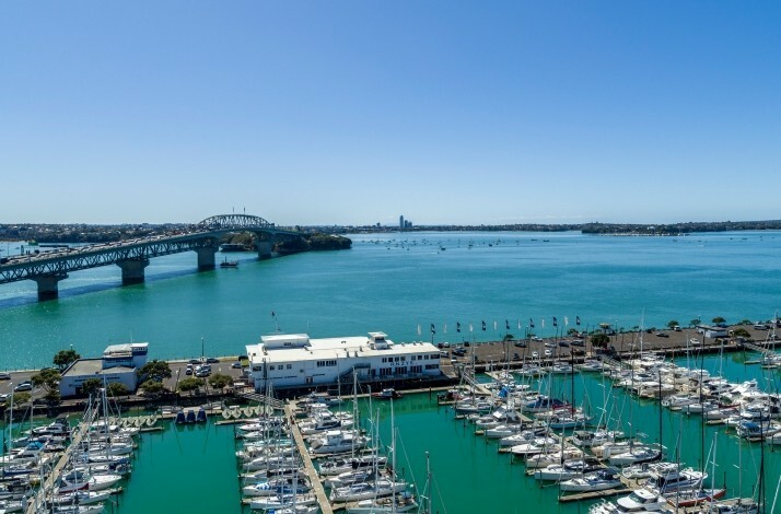 Bright daytime view of Westhaven Marina, Auckland Harbour Bridge, and turquoise waters with docked boats