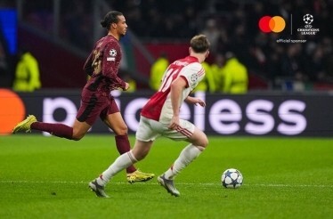Galatasaray A.S. and AFC Ajax players racing for the ball during UEFA Champions League 2025/26 league phase MD4, Mastercard logo and UEFA Champions League 'official sponsor' badge visible in the upper-right corner.