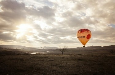 Hot air balloon with a priceless logo on it flying over field with river in Cappadocia.