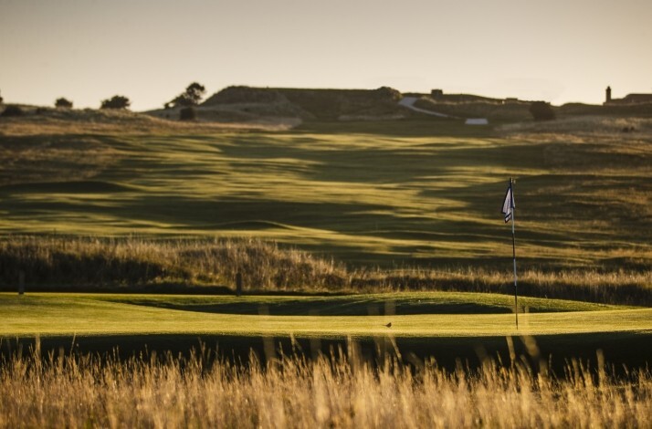 Gullane Golf Club fairway at golden hour, with a pin flag, fescue rough, and rolling links terrain stretching to the horizon.