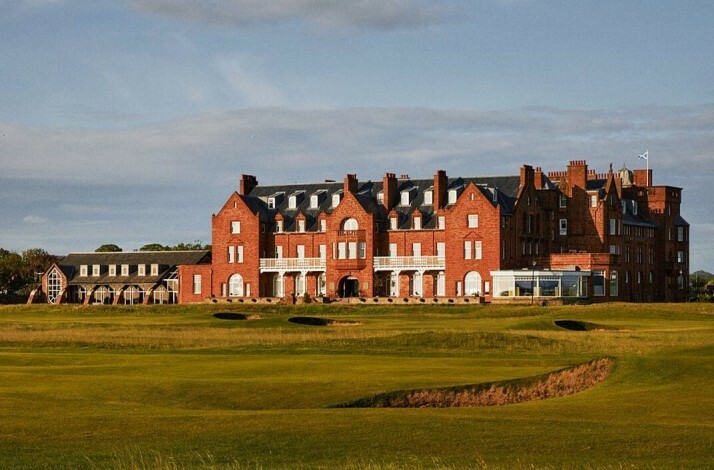 Large red-brick building with multiple chimneys overlooking a green golf course.