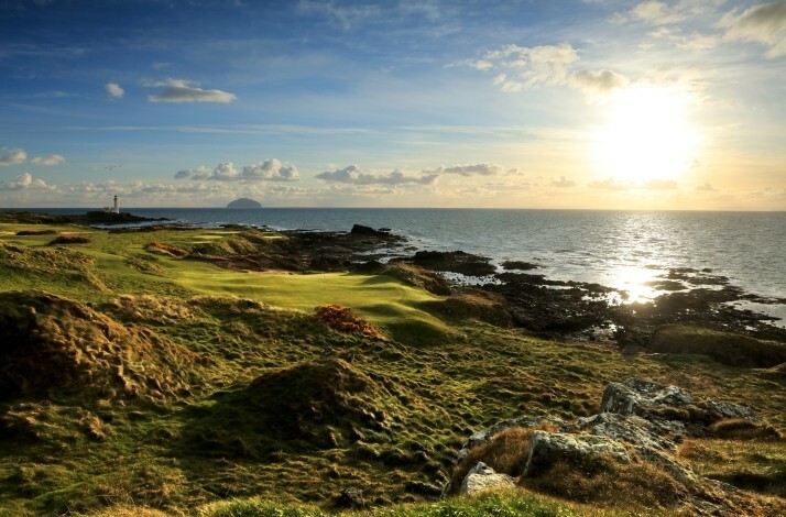 Sunlit coastal golf course with rocky shoreline and ocean views