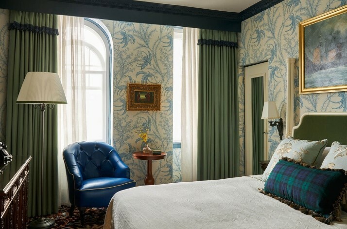Cozy hotel room with patterned wallpaper, green curtains, and a bed with decorative pillows