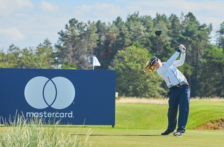 Golfer swinging a club on a green near a Mastercard sign