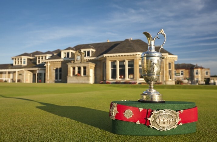 Silver trophy and red ceremonial belt displayed on a green lawn in front of a stone clubhouse.