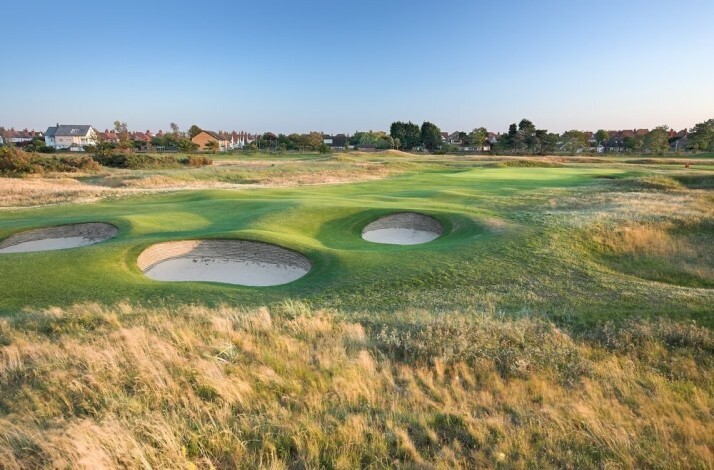 Scenic golf course with sandy bunkers near the coastline at sunset.