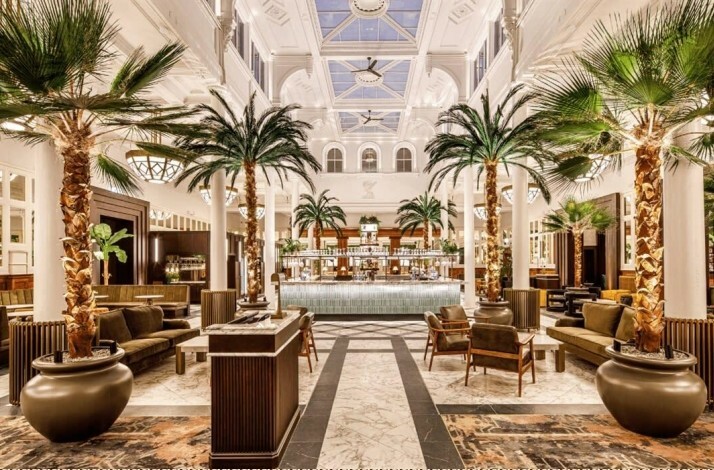 Opulent hotel lobby with a large bar and tropical palm trees.