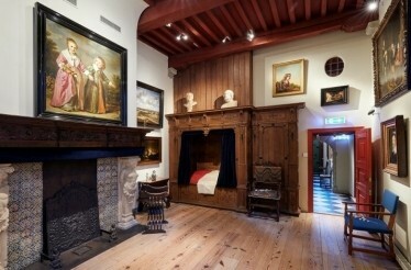 A bedroom with Rembrandt paintings on the walls and antique furniture in the Rembrandt House Museum.