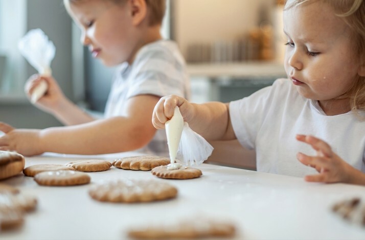 Children decorating cookies with icing on a table.
