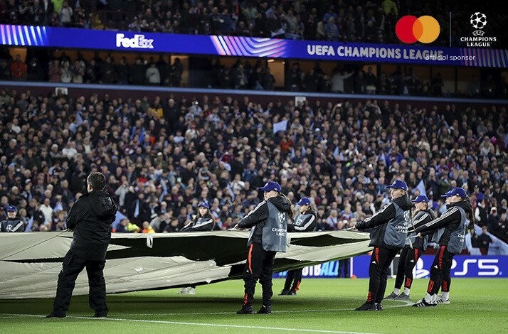 People on a football field holding a banner with an UEFA Champions League logo before a UEFA Champions League match