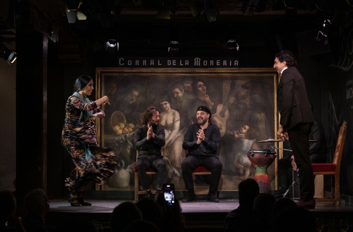 A lively flamenco performance at Corral de la Morería, with a vibrant dancer in motion and three musicians applauding enthusiastically onstage.