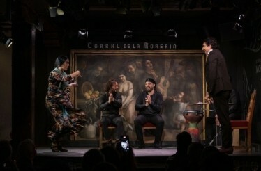 A lively flamenco performance at Corral de la Morería, with a vibrant dancer in motion and three musicians applauding enthusiastically onstage.