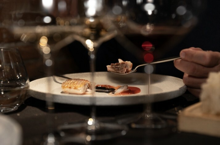 A dimly lit restaurant scene with a focus on a white plate of gourmet fish and sauce. 
