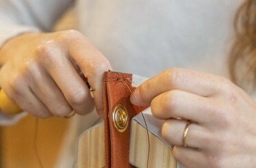 A close-up of woman’s hands in the process of stitching leather.