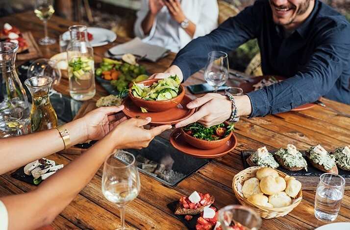 Person passing over a dish during dinner at EMIL restaurant in Dortmund. On the table there are various dishes, snacks and drinks.