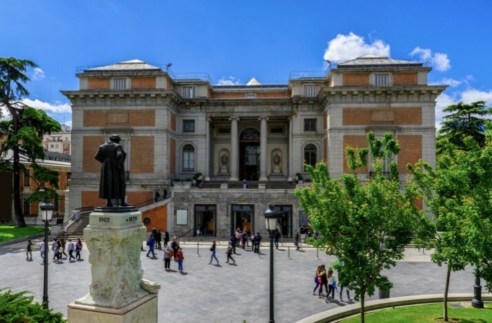 Exterior view of the Prado Museum in Madrid, featuring its grand architectural design and surrounding greenery.
