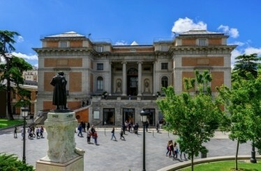 Exterior view of the Prado Museum in Madrid, featuring its grand architectural design and surrounding greenery.