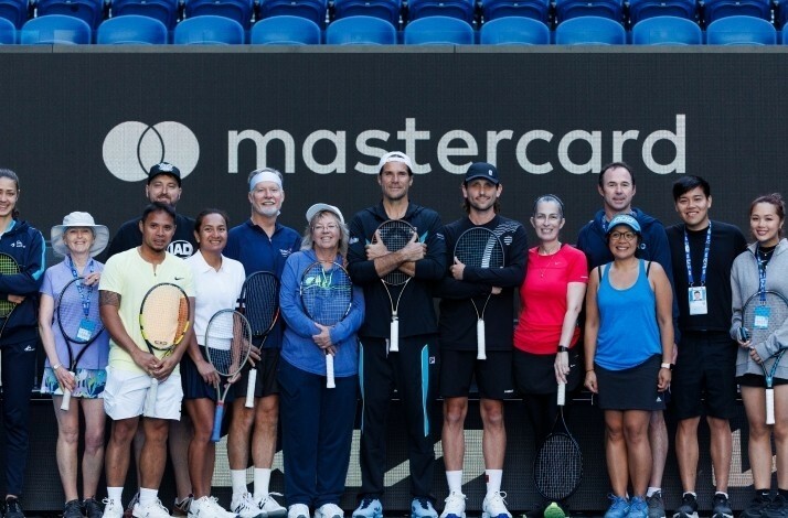 A group of players stands confidently on a tennis court, holding their rackets with a Mastercard banner in the background