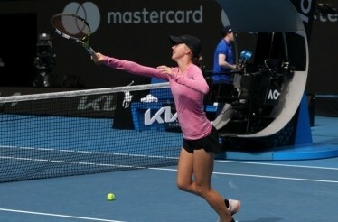 A tennis player on the court with their racket at arms length, a mastercard banner is in the background.