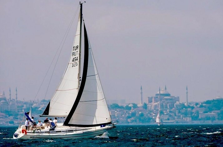 A white sailboat sailing on the Bosphorus in Istanbul, with the historic city skyline featuring Hagia Sophia and mosque minarets in the background.